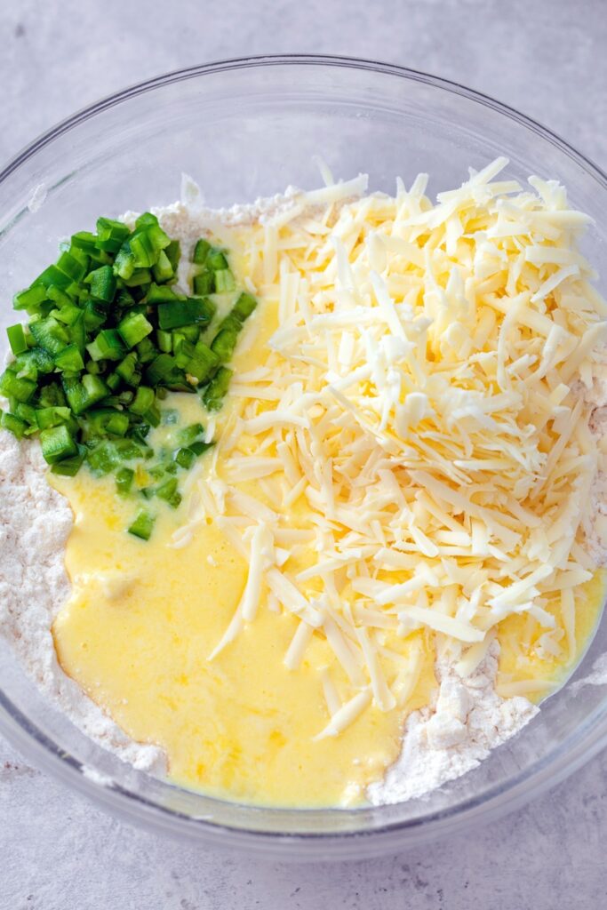 Overhead view of flour mixture with shredded cheddar, diced jalapeño and beaten eggs poured in