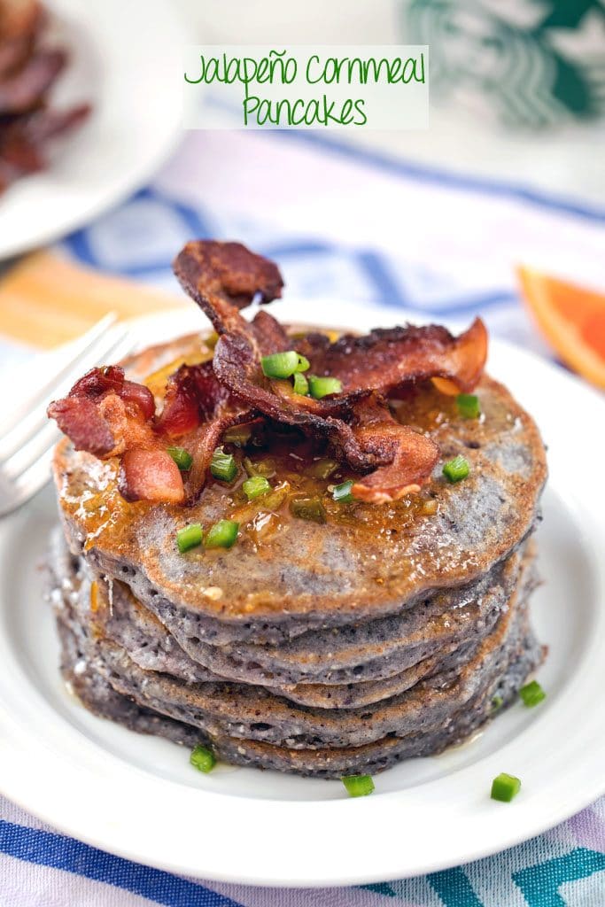 Hero image of blue jalapeño cornmeal pancakes in a large stack, topped with crispy bacon strips, orange syrup, and chopped jalapeño on a white plate with "Jalapeño Cornmeal Pancakes" text at top