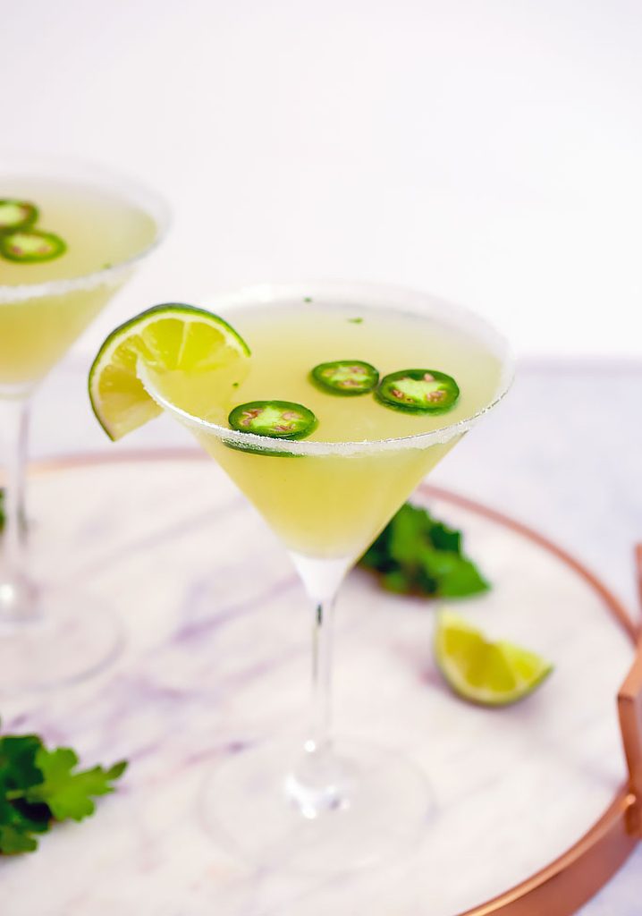 Head-on closeup view of jalapeño martini with vodka, parsley, lemon, and lime juice on a marble tray with lime wedge and parsley in background