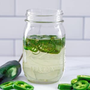 Head-on view of a mason jar filled with jalapeño simple syrup with sliced peppers in the syrup and all around jar