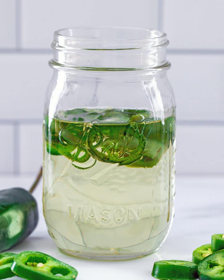 Head-on view of a mason jar filled with jalapeño simple syrup with sliced peppers in the syrup and all around jar