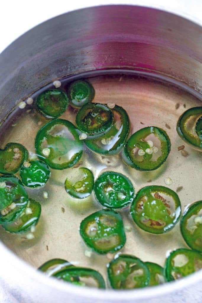 Overhead view of simple syrup simmering in saucepan with sliced jalapeño peppers