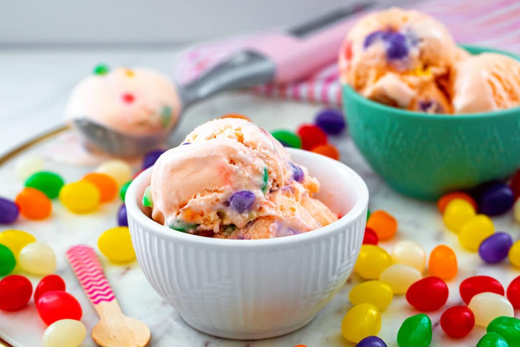 Landscape view of two bowls of jelly bean ice cream with jelly beans all around and scoop of ice cream in background.