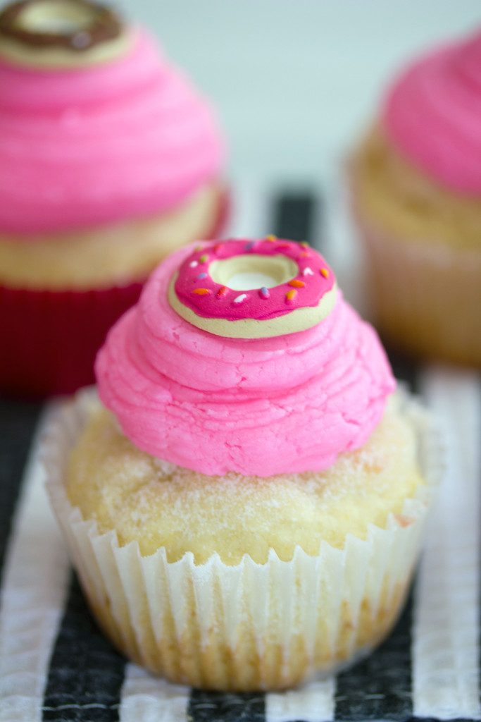 Head-on closeup view of a jelly doughnut cupcake with pink buttercream frosting and donut icing toppers