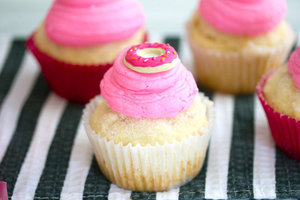 Landscape head-on view of multiple jelly doughnut cupcakes with pink buttercream frosting and donut icing toppers