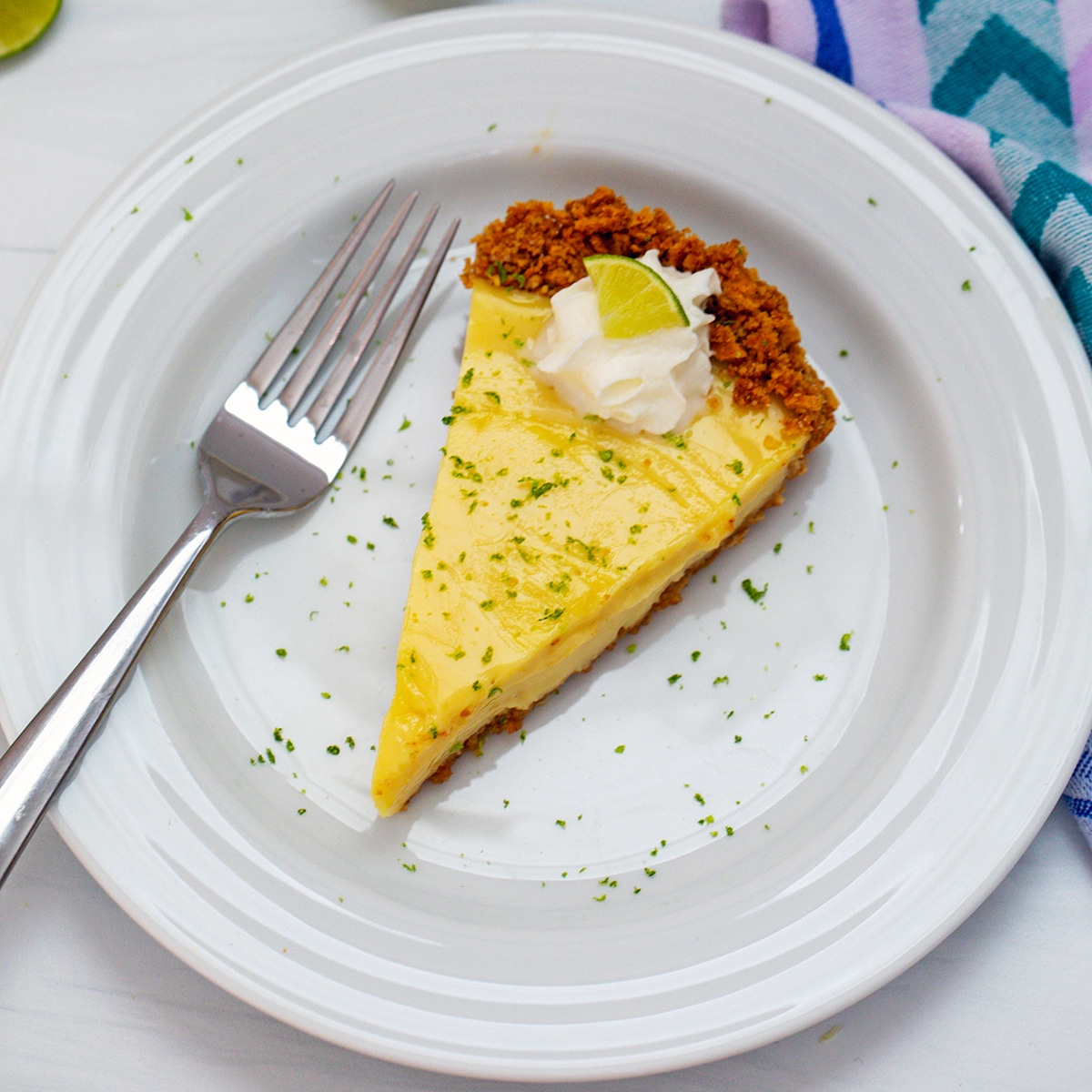 Overhead view of a slice of key lime pie with graham cracker crust and whipped cream on a white plate with a fork