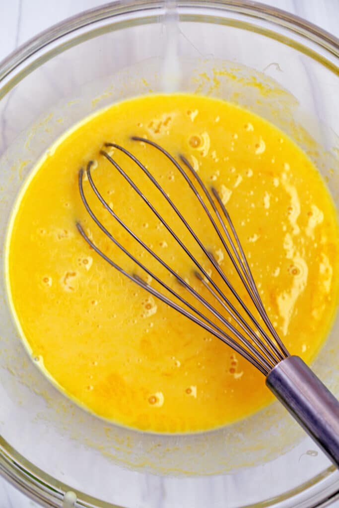 Egg yolks and condensed milk being whisked together in bowl