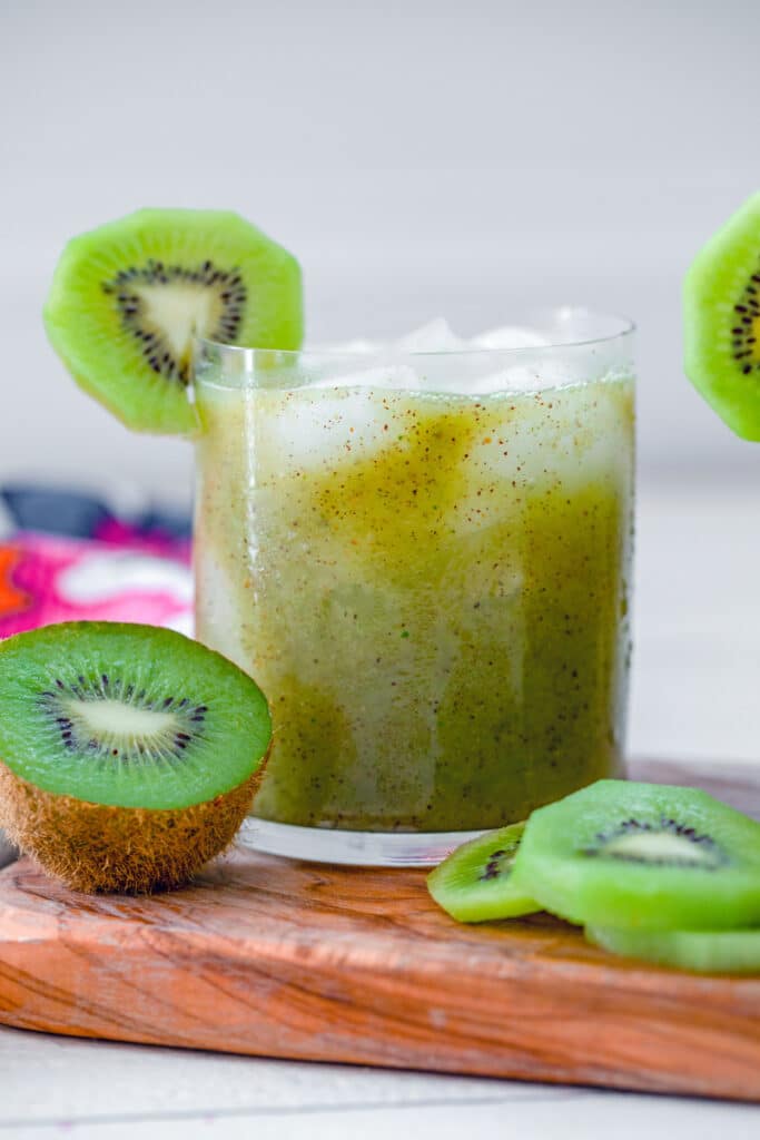 Head-on view of a kiwi mint tequila cocktail with kiwi fruit all around 