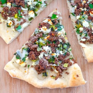 Slice of lamb flatbread topped with mint and feta pulled out from the rest of the pizza