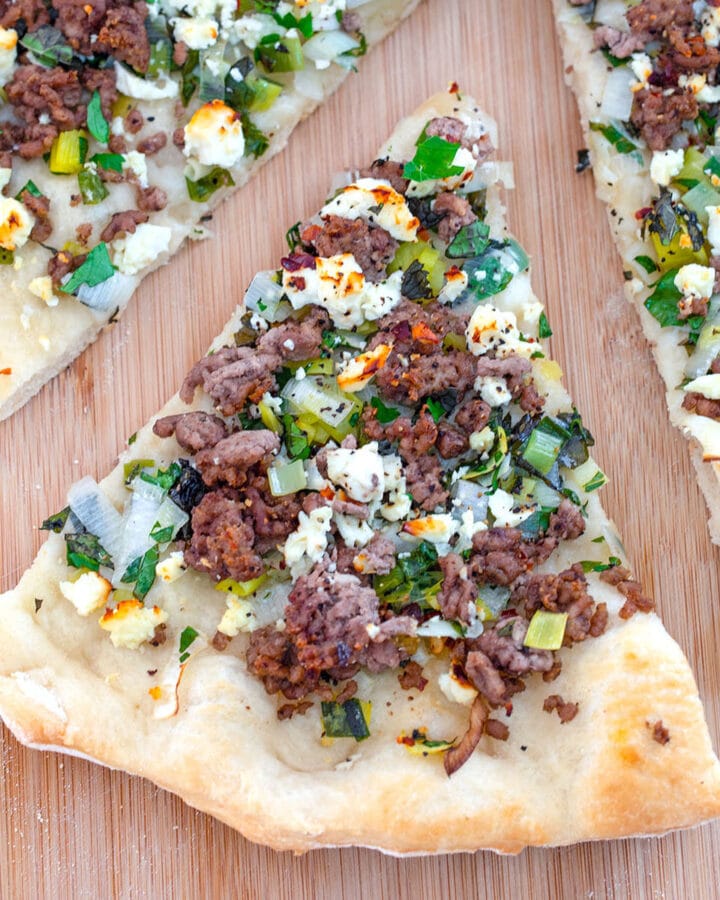 Slice of lamb flatbread topped with mint and feta pulled out from the rest of the pizza