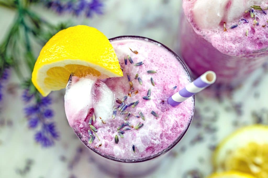Landscape bird's eve view of a lavender lemonade float with dried lavender sprinkled on top, a lemon wedge garnish, and a striped straw