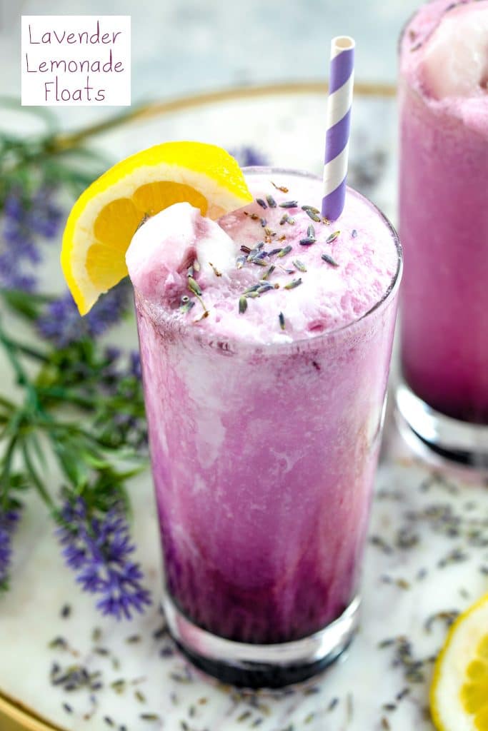 Overhead view of a purple lavender lemonade float in a tall glass with lemon wedge garnish, dried lavender, and striped straw, with lavender and a second drink in the background and recipe title at top