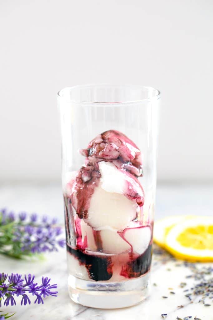 Head-on view of a tall glass filled with lemon sorbet and lavender simply syrup drizzled over it
