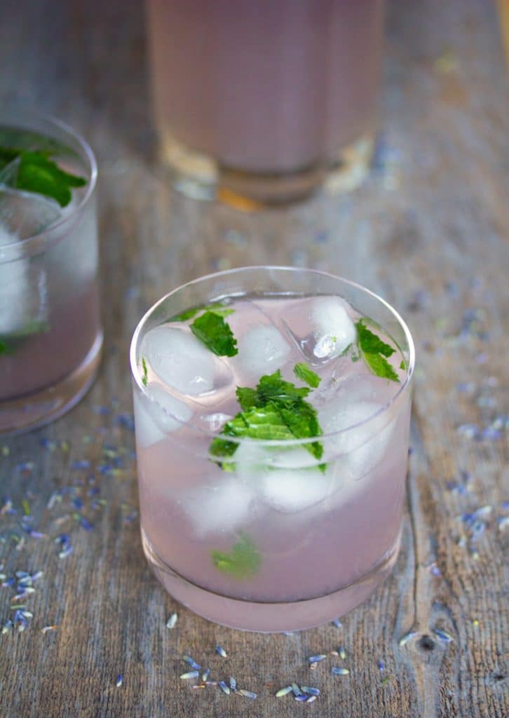 Un verre de mojitos à la limonade de lavande sur une surface en bois avec de la lavande séchée saupoudrée autour de