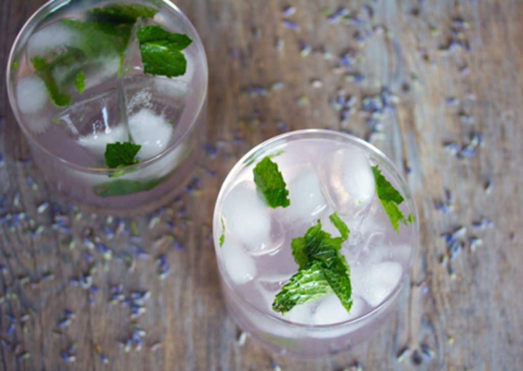 Landschaftsfoto mit einer Vogelperspektive von zwei Lavendel-Limonaden-Mojito-Cocktails auf einer Holzoberfläche mit getrocknetem Lavendel's eye view of two lavender lemonade mojito cocktails on a wooden surface with dried lavender sprinkled around