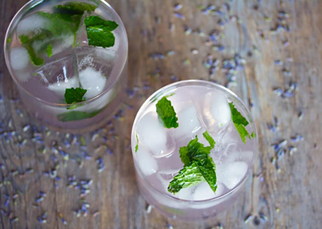 Landscape photo with a bird's eye view of two lavender lemonade mojito cocktails on a wooden surface with dried lavender sprinkled around