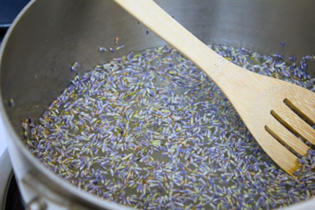 di lavanda Secchi in una pentola con l'acqua e lo zucchero nel processo di diventare lavanda sciroppo semplice