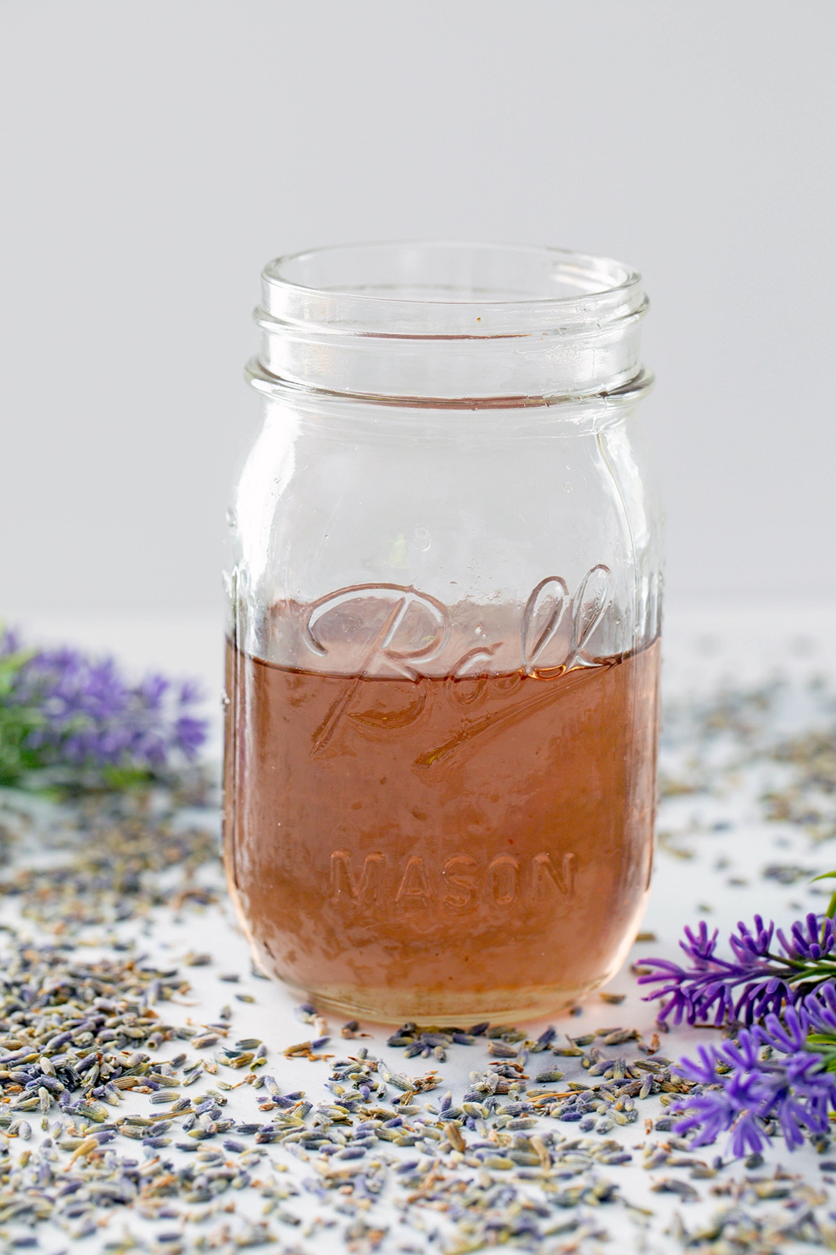 Mason jar filled with lavender simple syrup with lavender buds all around.