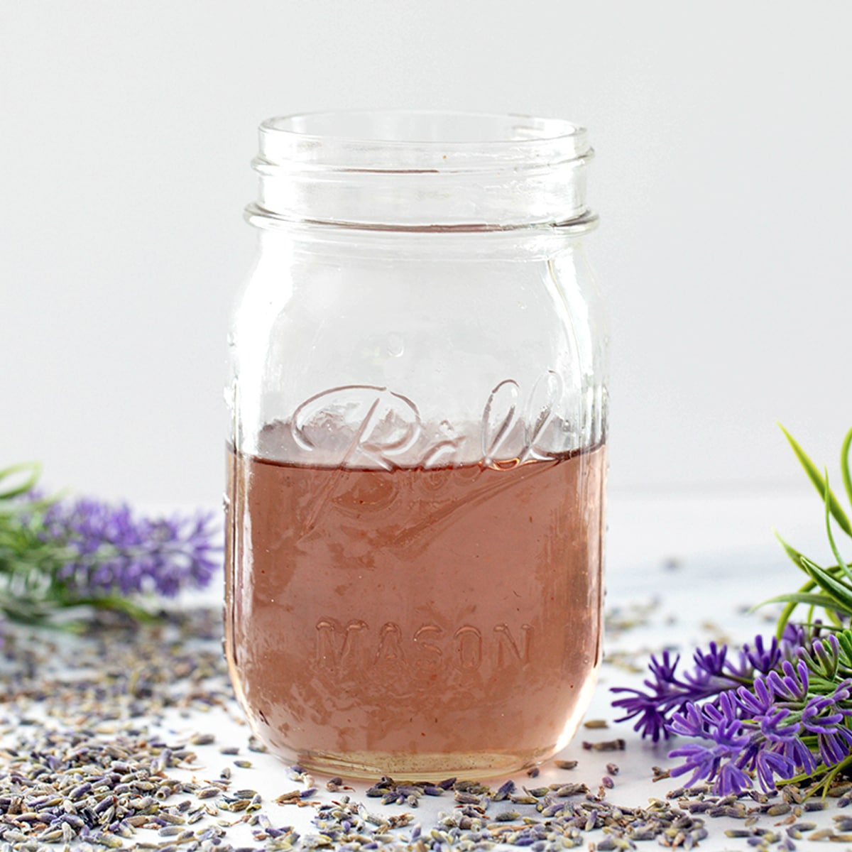 Head-on view of a mason jar of lavender simple syrup with lavender flowers all around