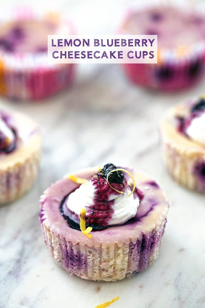 A plate full of Lemon Blueberry Cheesecake Cups topped with whipped cream, wild blueberry sauce, and lemon zest with text on the photo that says "Lemon Blueberry Cheesecake Cups"