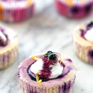 An up-close view coming from above of a lemon blueberry cheesecake cup with whipped cream topping, blueberry sauce, and lemon zest