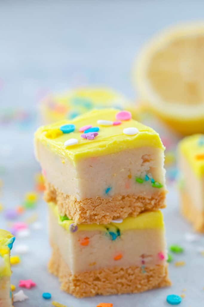 Close-up of two lemon cookie dough bars stacked on each other surrounded by colorful sprinkles and with a lemon half in the background