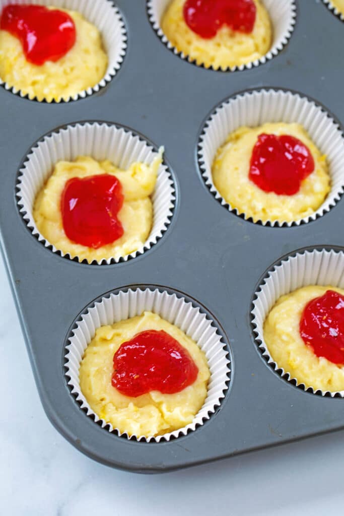Lemon batter in cupcake tin with raspberry jam on top of each