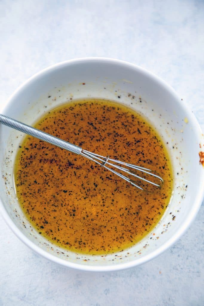 Overhead view of white bowl with lemon dressing and little whisk