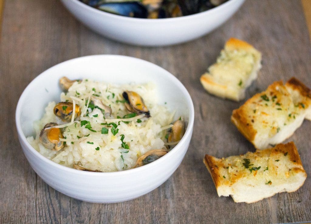 Landscape view of a small white bowl of lemon and fennel risotto with mussels with pieces of garlic bread on the side