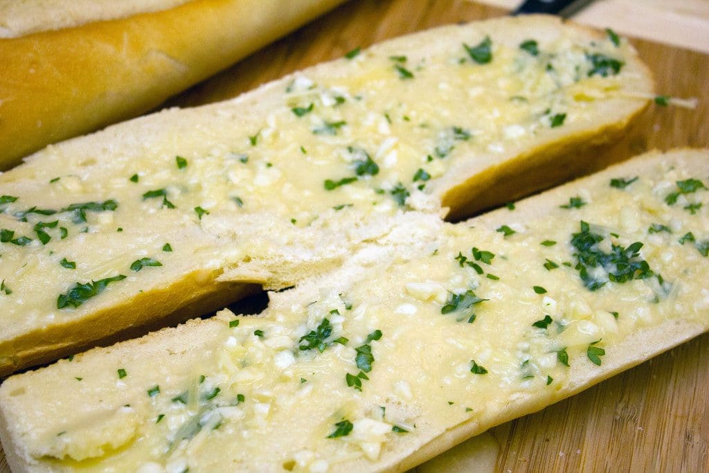 Overhead view of garlic bread with lots of parsley on a cutting board 