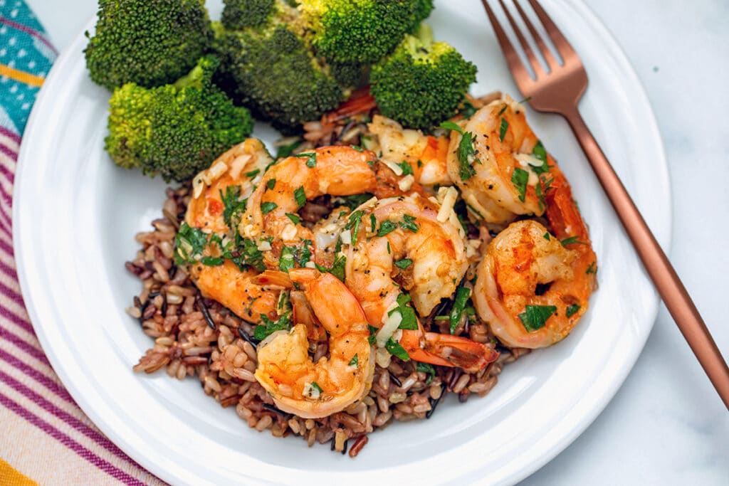 Landscape view of lemon garlic parmesan shrimp over a bed of rice with broccoli and a rose gold fork