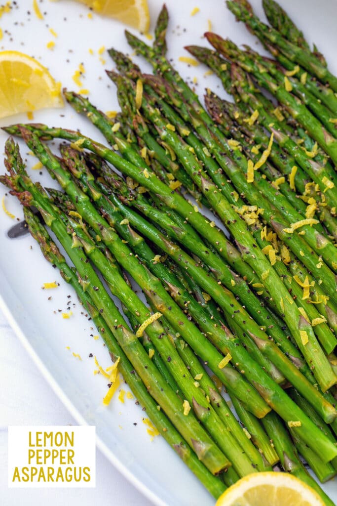 Overhead closeup of lemon pepper asparagus on a platter with lemon wedges and zest and recipe title at bottom.