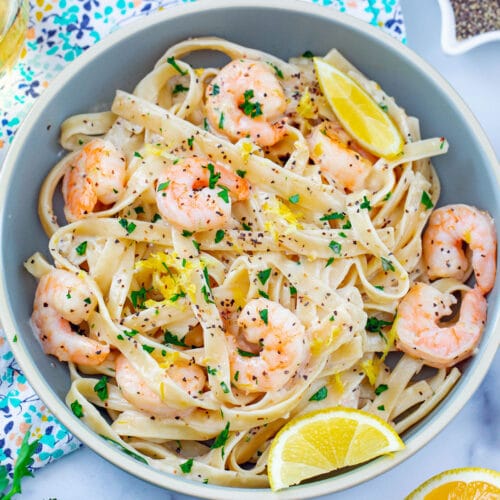 Overhead close-up view of lemon pepper pasta with shrimp topped with lemon zest, chopped parsley, and lemon wedges.