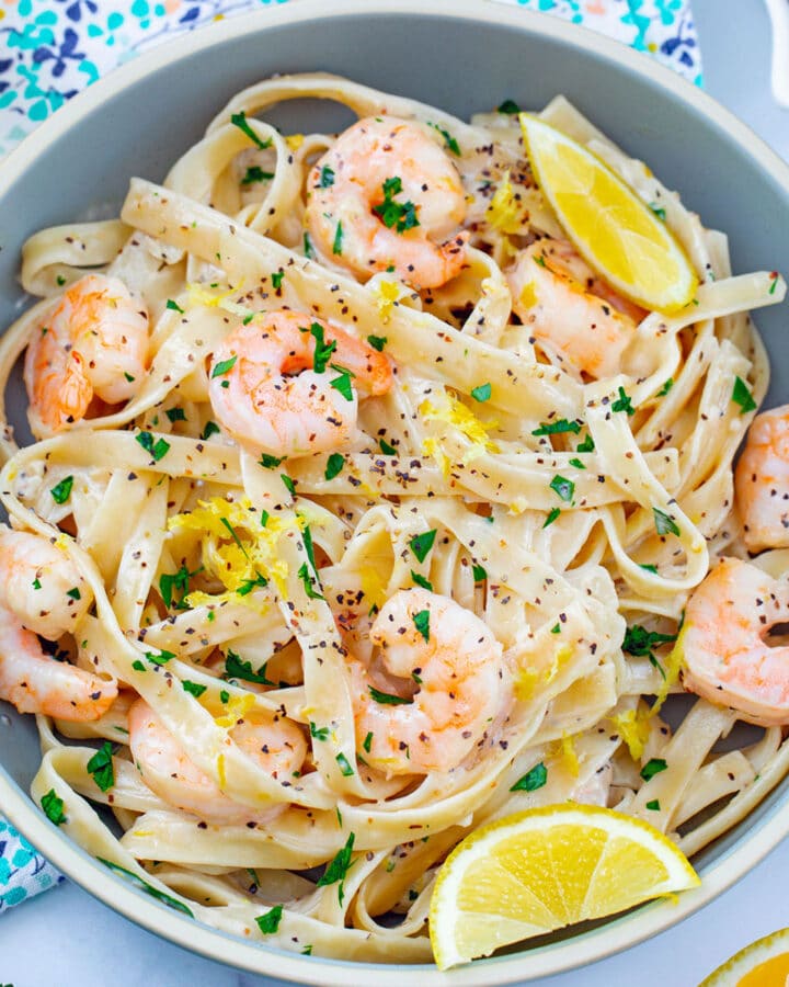 Overhead close-up view of lemon pepper pasta with shrimp topped with lemon zest, chopped parsley, and lemon wedges.