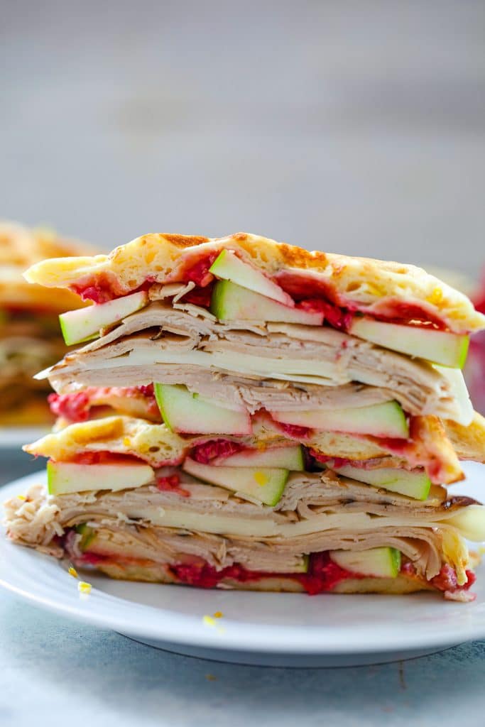 Head-on view of lemon waffle sandwiches sliced in half and stacked on top of each other and filled with turkey, cheese, green apple, and raspberry spread