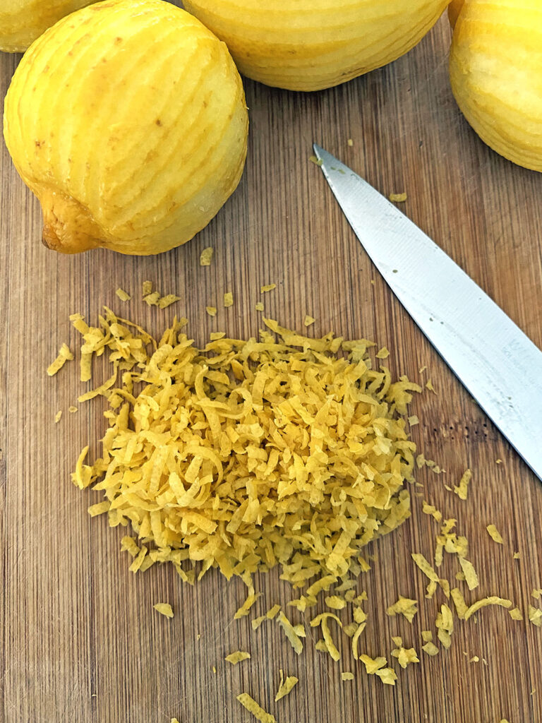 Lemon zest on cutting board with lots of lemons in background