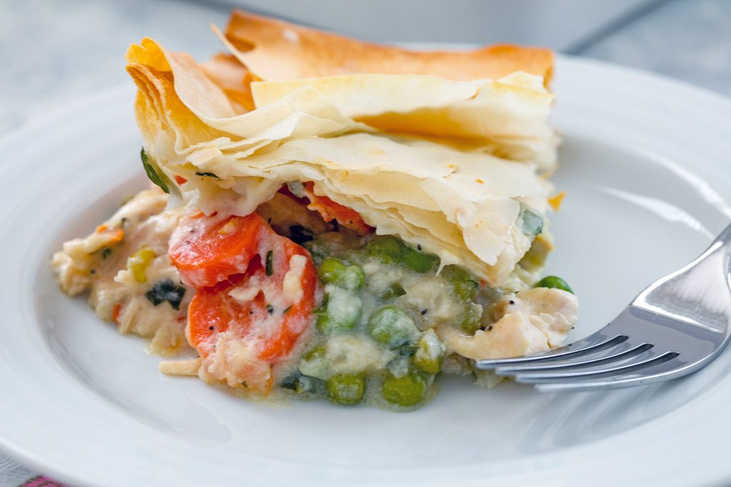 Landscape close-up head-on view of lighter chicken pot pie with peas and carrots on a white plate with a fork