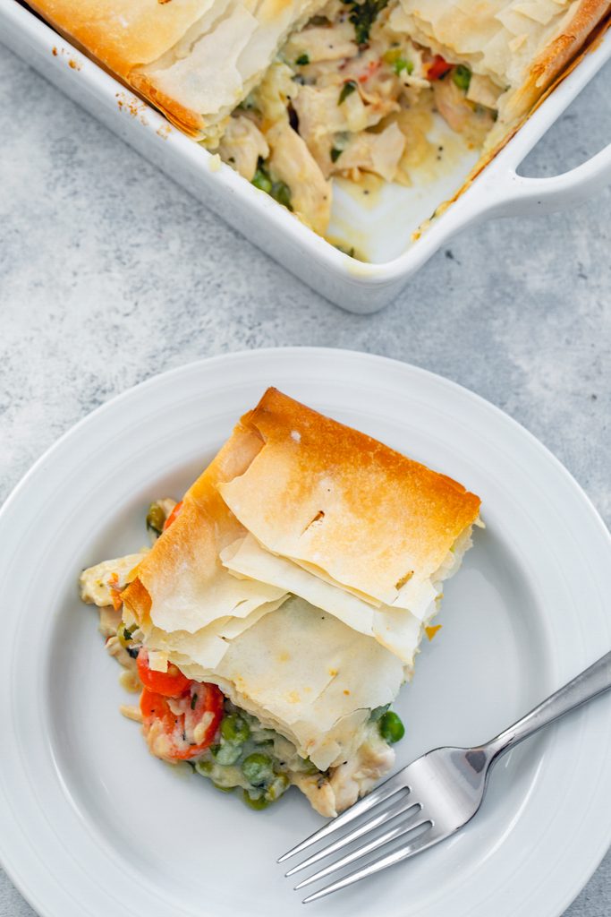 Bird's eye view of lighter chicken pot pie serving on a white plate with a fork with baking dish in the background