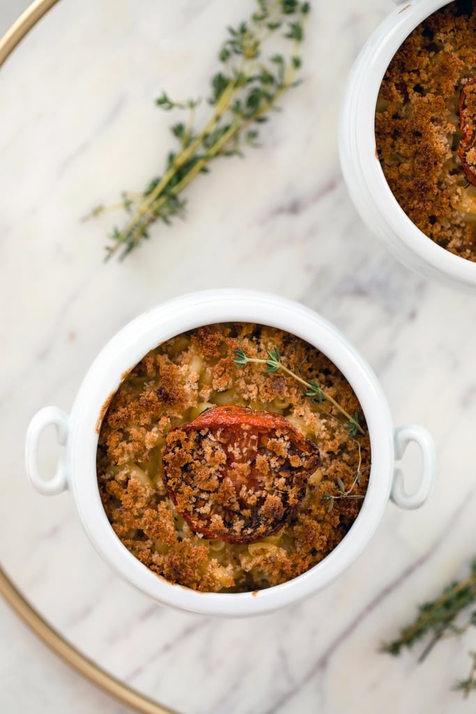 Overhead view of a white ramekin of mac and cheese with roasted tomatoes with thyme sprig on the side.