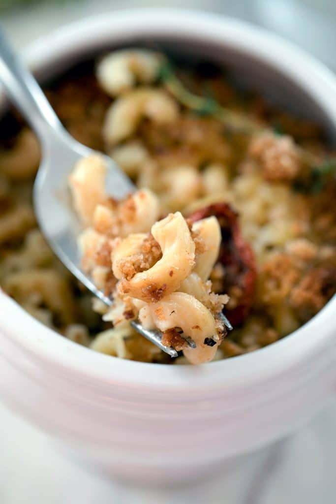 Overhead view of a white ramekin of lighter macaroni and cheese with a forkful of mac and cheese being held up