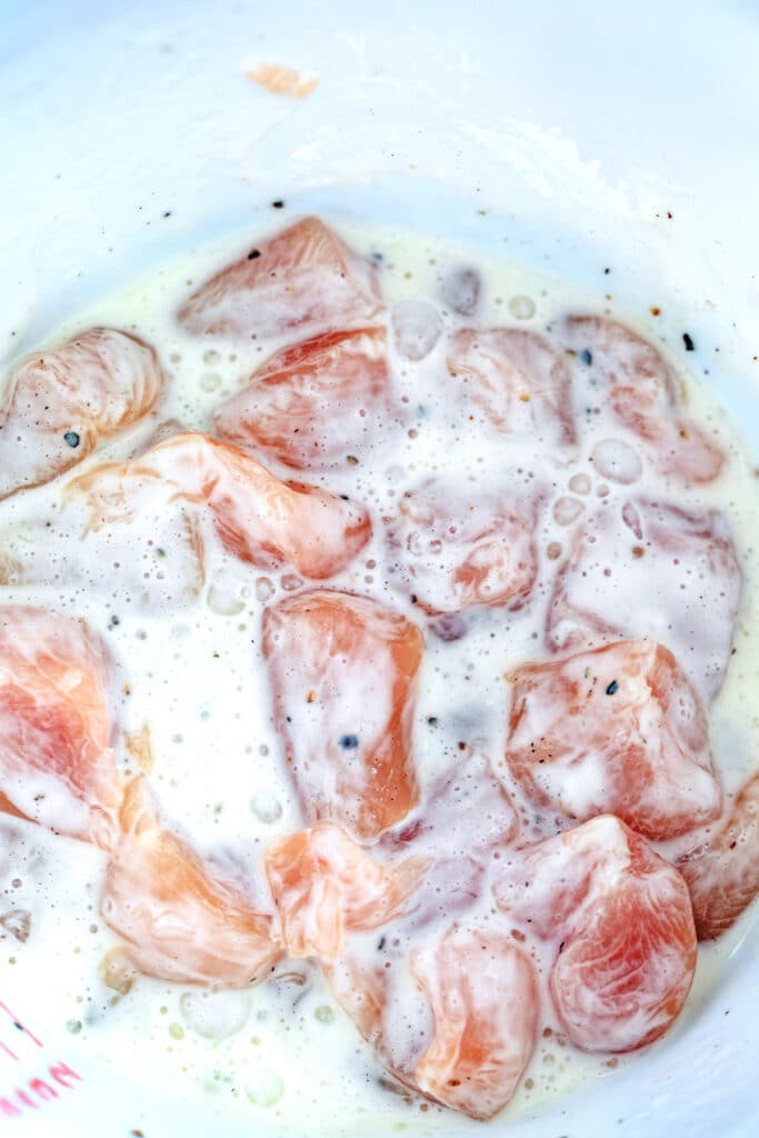 Cubed chicken tossed in egg whites and cornstarch in bowl.