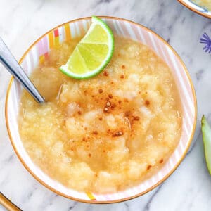 Bird's eye closeup view of lime ginger pear sauce in a bowl with ground ginger, lime wedge, and spoon.