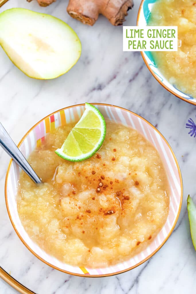 Overhead view of lime ginger pear sauce in a bowl topped with ground ginger and lime wedge with second bowl and pear half and fresh ginger in the background with recipe title at top.