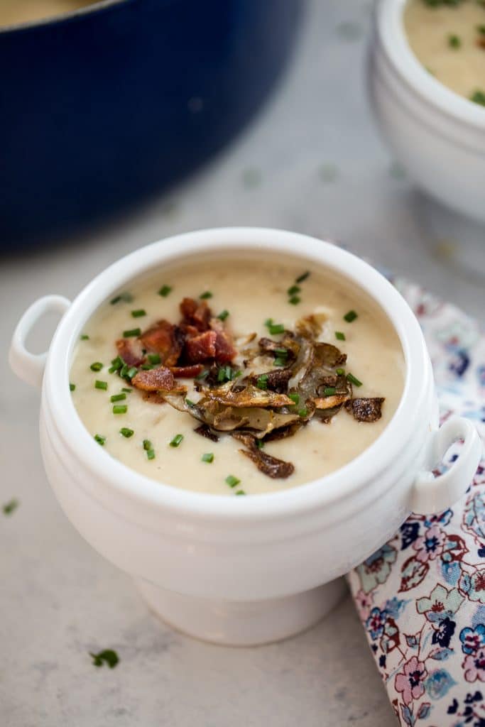 Closeup head-on view of a white bowl of loaded baked potato soup with crispy potato skins and bacon and chives on top