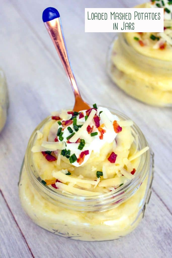 Overhead view of a small mason jar filled with mashed potatoes and topped with cheese, sour cream, chives, and crumbled bacon with a small gold fork sticking out of it, another jar in the background, and recipe title at top