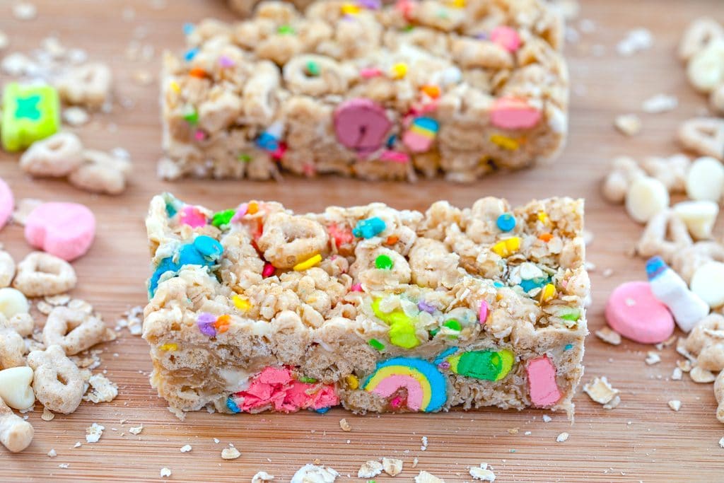 Landscape close-up view of a Lucky Charms granola bar on a wooden board surrounded by Lucky Charms cereal and oats