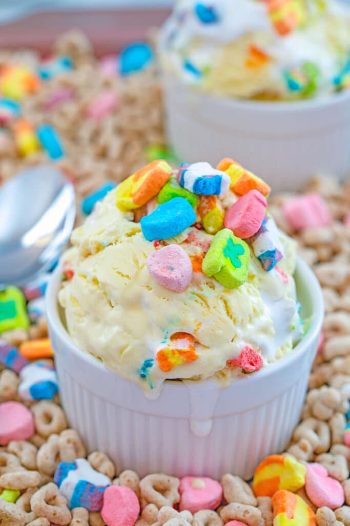 Overhead view of a white bowl of Lucky Charms ice cream topped with extra marshmallows on a bed of Lucky Charms cereal.