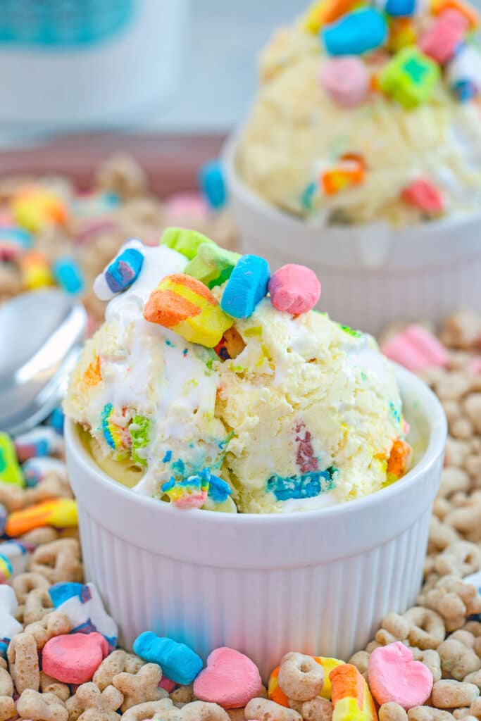 Overhead close-up view of Lucky Charms ice cream in a white bowl topped with marshmallows on a bed of cereal with second bowl of the background