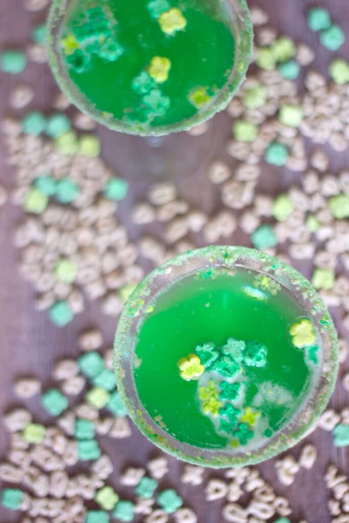 Bird's eye view of two green Lucky Charms martinis with cereal scattered all around