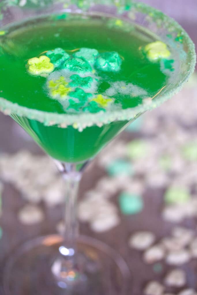 Close-up of a green Lucky Charms martini with green marshmallows and cereal scattered all around